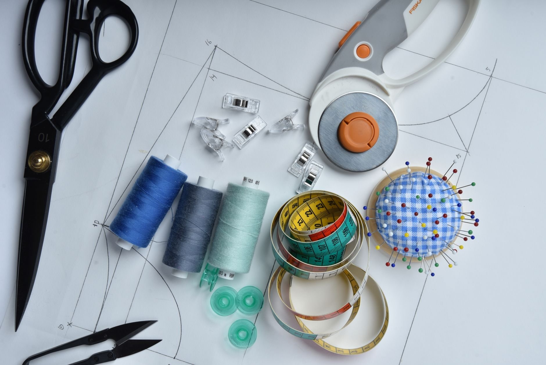 A collection of sewing tools including scissors, thread, and rotary cutter on pattern paper, perfect for tailoring.