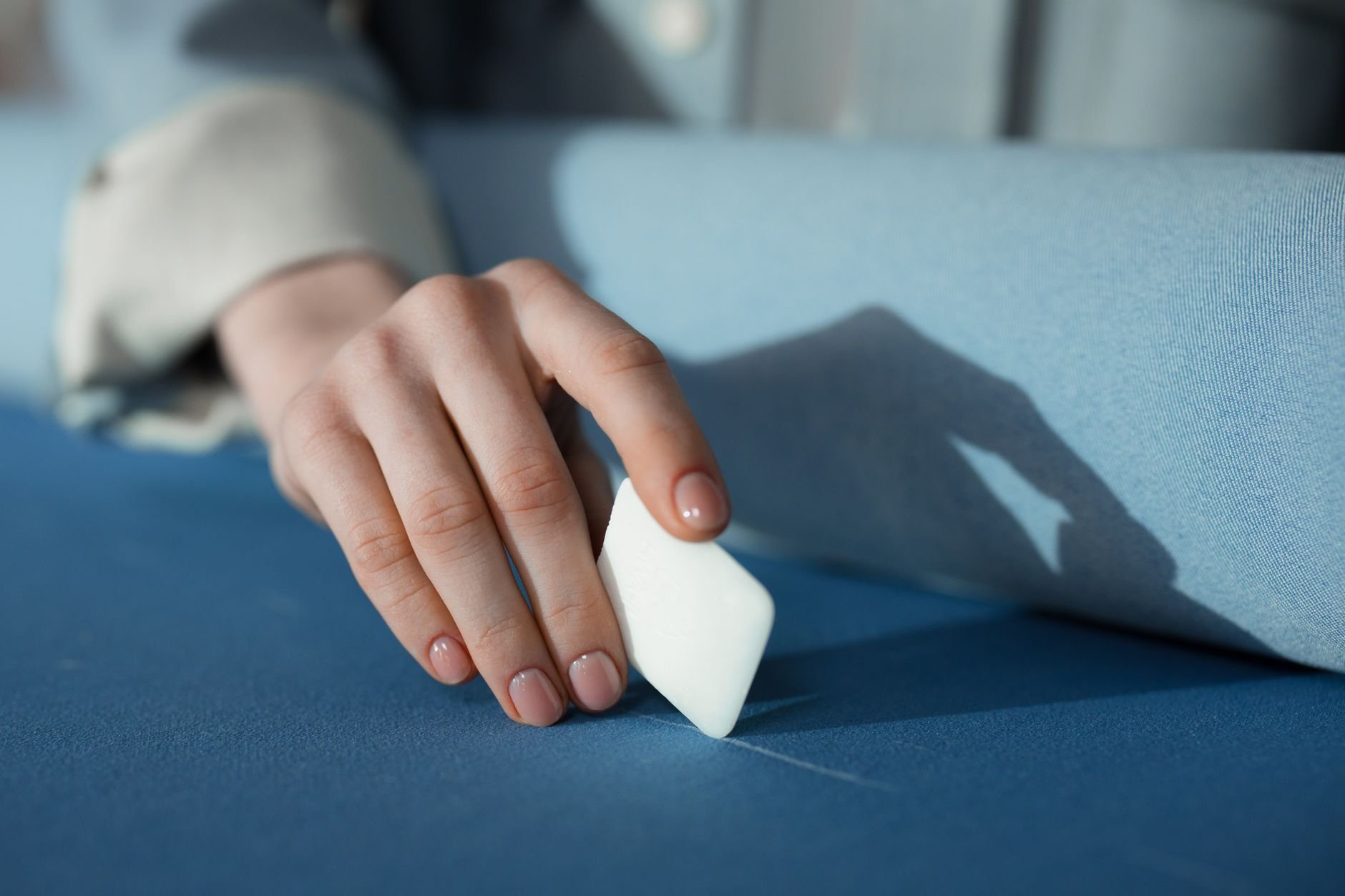 A detailed close-up of a person's hand using tailor's chalk on blue fabric in a sewing setting.